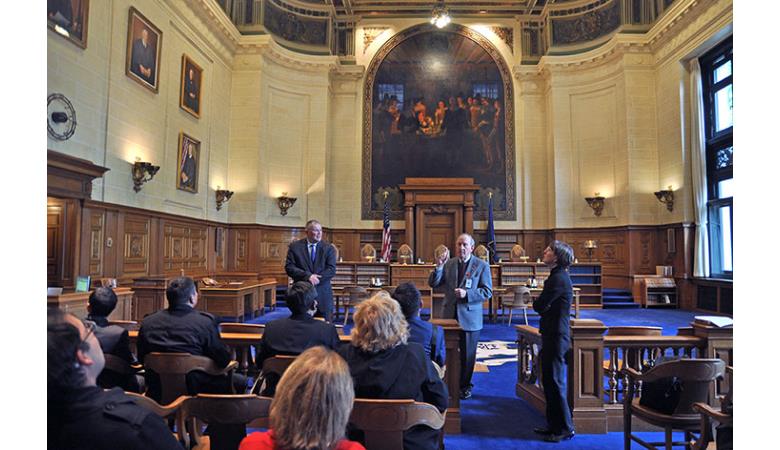 Supreme Court Justice Dennis G. Eveleigh looks on as Supreme Court guide Phil Cocchiola provides information about the<br>Supreme Court Courtroom to the delegation from the Kyrgyz Republic.